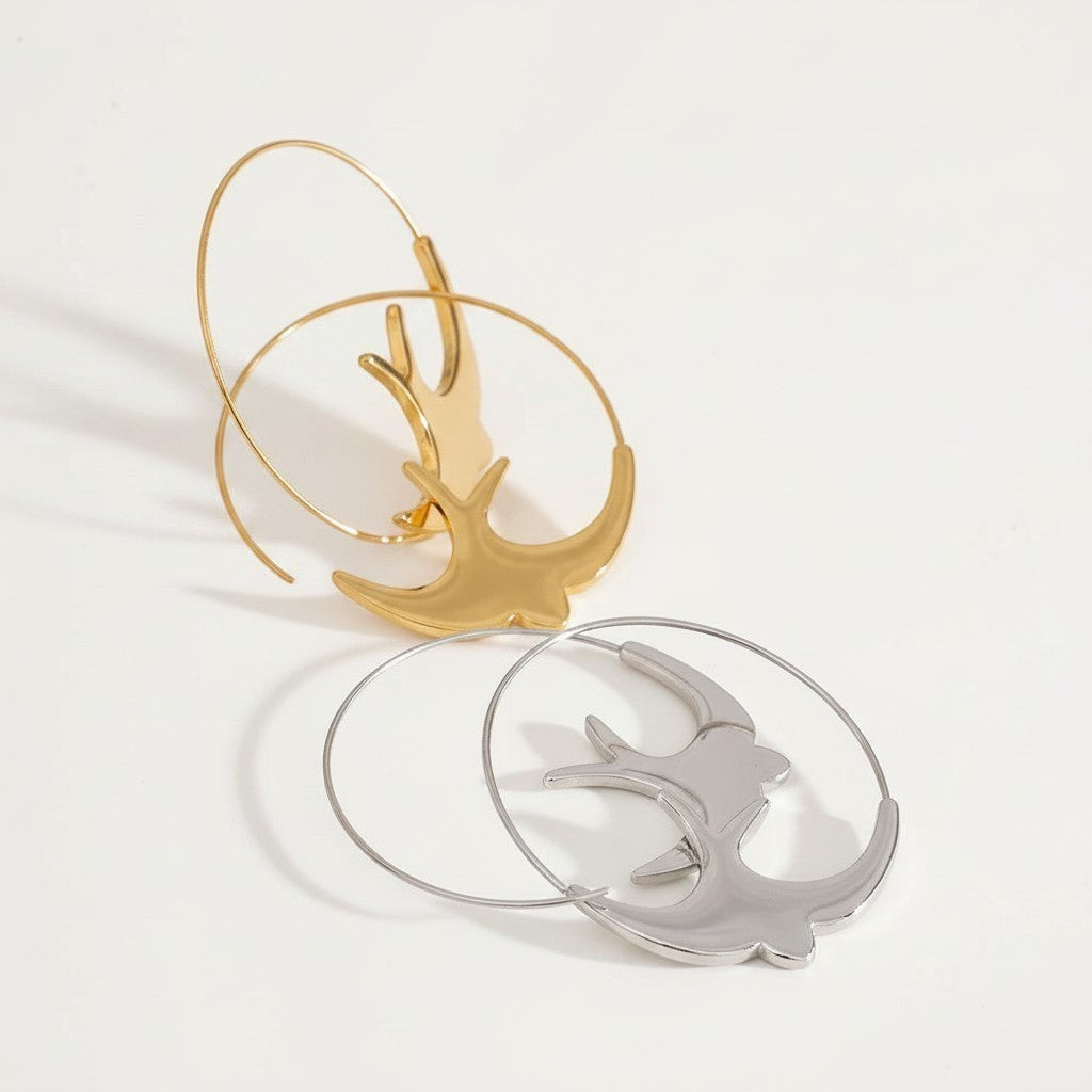 PRO RAY ALYRA sculptural hoop earrings in gold and silver finishes, featuring a swallow silhouette.
