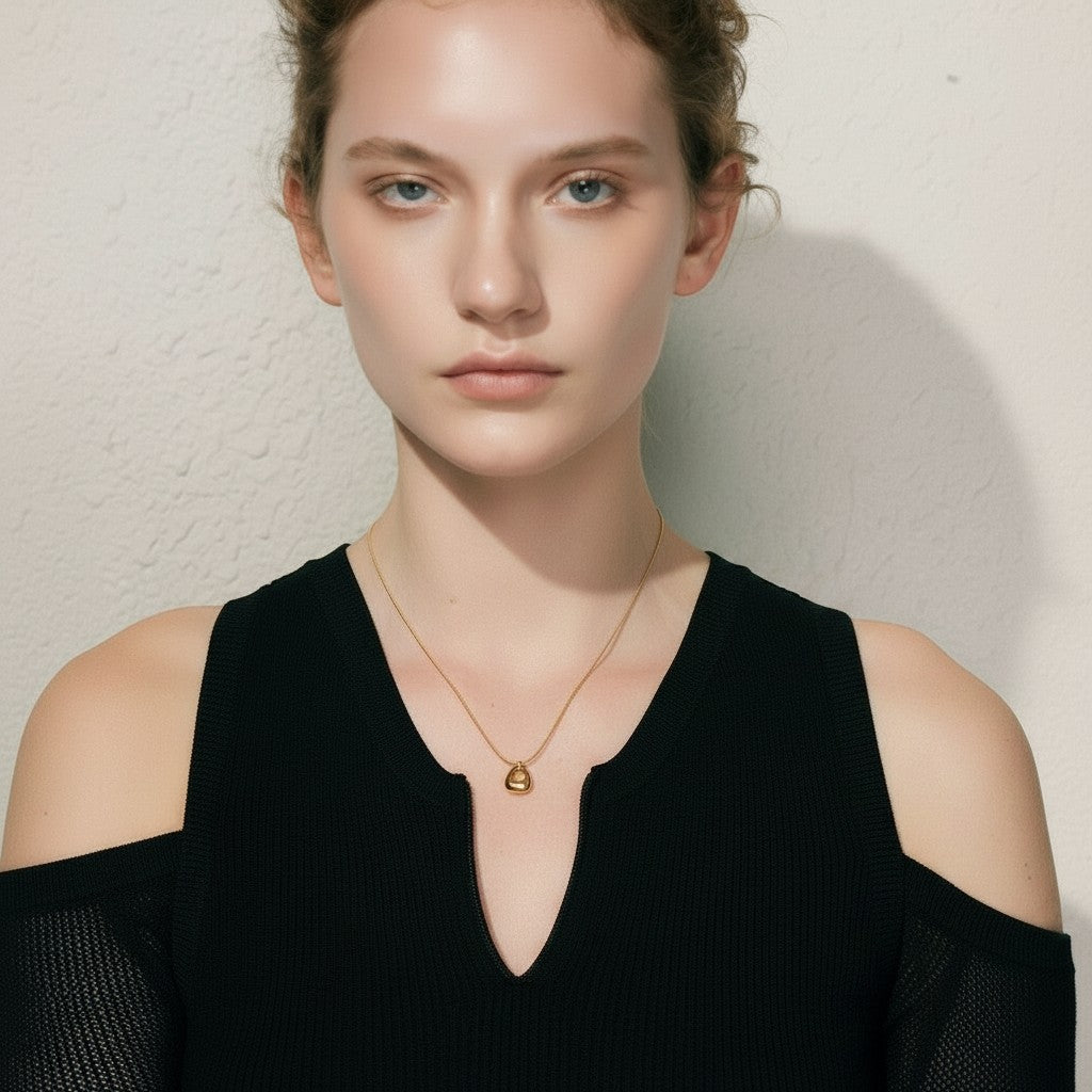 PRO RAY gold geometric pendant necklace on a woman with blue eyes and fair skin, wearing a black top.
