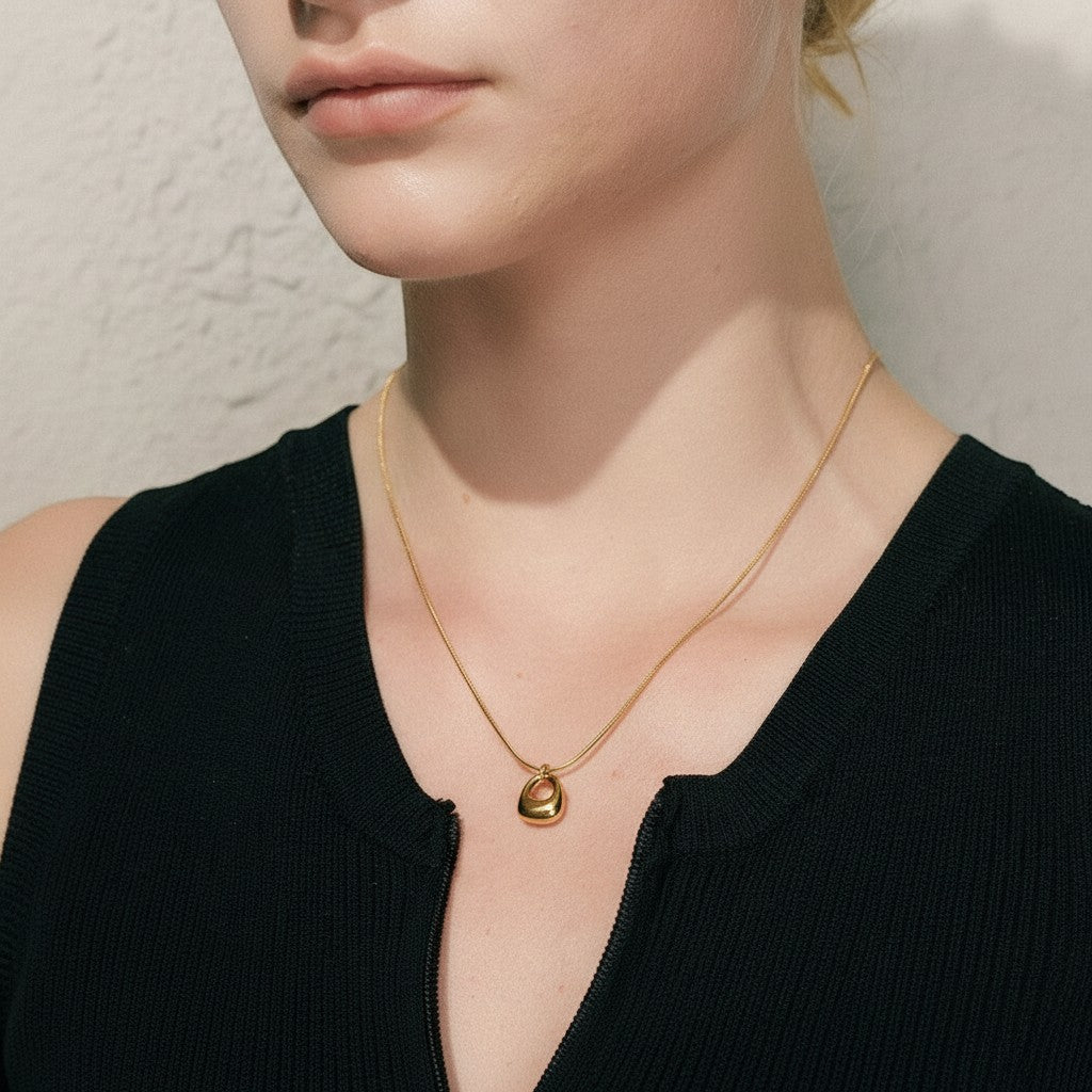 PRO RAY gold geometric pendant necklace on a thin chain, worn by a woman with blue eyes and blonde hair.